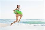 Pretty young woman holding a rubber ring while jumping on beach and looking at camera