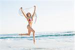 Smiling slender woman jumping in the air holding shawl on the beach