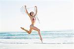 Happy slender woman jumping in the air holding shawl on the beach