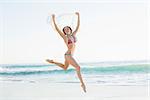 Euphoric slender woman jumping in the air holding shawl on the beach