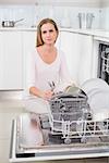 Serious gorgeous model kneeling behind dish washer in bright kitchen