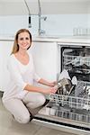 Lucky gorgeous model kneeling next to dish washer in bright kitchen