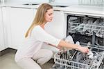 Calm gorgeous model kneeling next to dish washer in bright kitchen