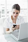 Brunette businesswoman messaging with her smartphone sitting at her desk