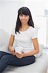 Lovely smiling woman holding a cup smiling at camera sitting on couch