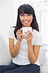 Calm beautiful woman holding a cup smiling at camera sitting in bright living room