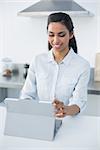 Lovely smiling woman using her tablet standing in bright kitchen at home