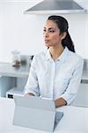 Calm thinking woman using her tablet standing in kitchen at home