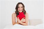 Portrait of a smiling young woman sitting with a hot water bottle in bed