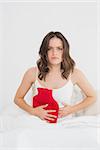 Portrait of an upset young woman sitting with a hot water bottle in bed