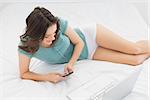 Casual young woman text messaging by laptop in bed at home