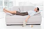 Side view of a young woman with laptop sleeping on sofa at home