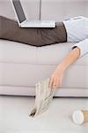 Mid section of a young woman with laptop and news paper lying on sofa at home
