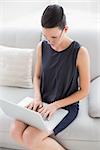 Beautiful well dressed young woman using laptop on sofa at home