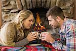 Side view of a romantic young couple with tea cups in front of lit fireplace