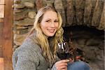 Close up portrait of a beautiful woman with wineglass in front of lit fireplace
