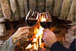 Close up of hands toasting wineglasses in front of lit fireplace