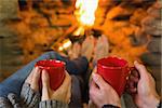 Close up of hands holding red coffee cups in front of lit fireplace