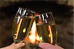 Close up of hands toasting champagne flutes in front of lit fireplace