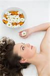 Close up of a beautiful young woman lying with bowl of flowers in beauty salon