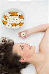 Close up of a beautiful young woman lying with bowl of flowers in beauty salon