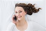High angle portrait of a young brunette using mobile phone in bed at home