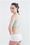 Rear view portrait of a toned young woman with hands on hips against wall in fitness studio