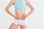 Mid section of a fit woman in sportswear with hands on belly against wall in fitness studio