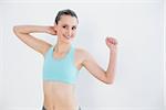 Portrait of a smiling toned young woman stretching hands against wall in fitness studio