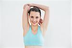 Portrait of a toned young woman stretching hands behind head against wall in fitness studio