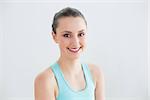 Close up portrait of a smiling toned young woman against wall in fitness studio