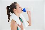 Side view of a fit young woman drinking water at the gym after working out