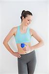 Toned young woman holding water bottle against wall at fitness studio