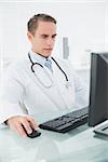 Serious male doctor using computer at medical office