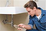 Young male plumber with wrench by sink in bathroom at home