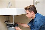 Side view of a handsome plumber repairing the drain of sink in bathroom