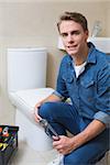 Portrait of a smiling handsome plumber with toolbox doing toilet reparation