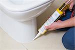 Close up of a plumber fixing toilet in a washroom with silicone cartridge