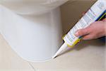 Close up of a plumber fixing toilet in a washroom with silicone cartridge