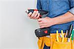 Close up mid section of a handyman with drill and toolbelt by the wall