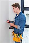 Handsome young handyman using a drill with toolbelt around waist
