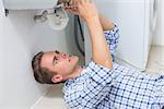 Side view of a young plumber repairing washbasin drain in bathroom