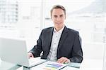 Portrait of a smiling young businessman with laptop sitting at office desk