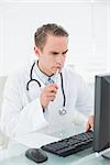 Serious male doctor with pen looking at computer in medical office