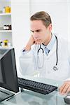 Serious male doctor using computer at medical office