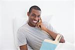 Portrait of a smiling young Afro man with a book in bed at house