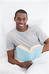 Portrait of a smiling young Afro man with a book in bed at house