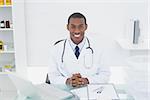 Portrait of a smiling male doctor with laptop sitting at medical office