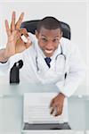 Overhead portrait of a smiling male doctor with laptop gesturing okay sign at medical office