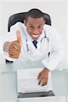 Overhead portrait of a smiling male doctor with laptop gesturing thumbs up at medical office